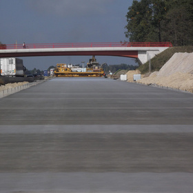 Frisch hergestellte Fahrbahnfläche mit Baumaschinen, im Hintergrund eine Brücke