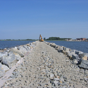 Steindamm im Wasser mit Baumaschine im Hintergrund