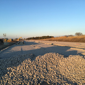 Großflächige Baustelle mit aufgeschütteter Schotterfläche, Gleisen und Baumaschinen