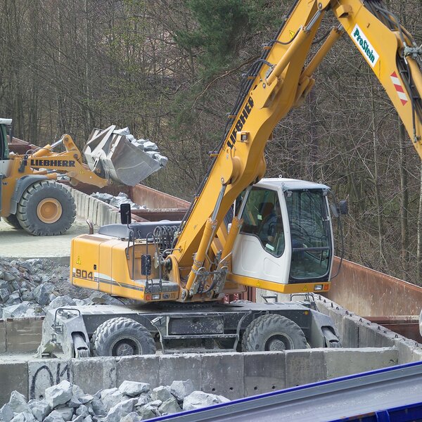 Radlader und Bagger verladen Schotter in Eisenbahnwaggons