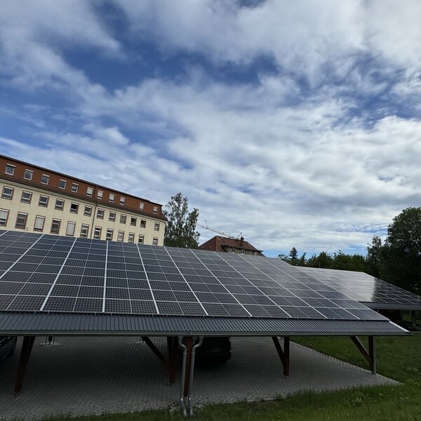 Photovoltaikanlage auf einem Carport vor historischem Gebäudekomplex