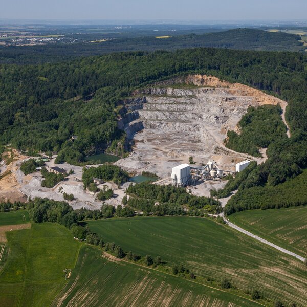 Luftaufnahme eines großflächigen Steinbruchs am Berghang, umgeben von Wald und Feldern