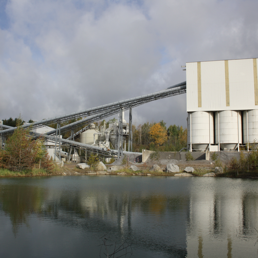 Aufbereitungsanlage mit Förderbändern und Silos am Rande eines Sees