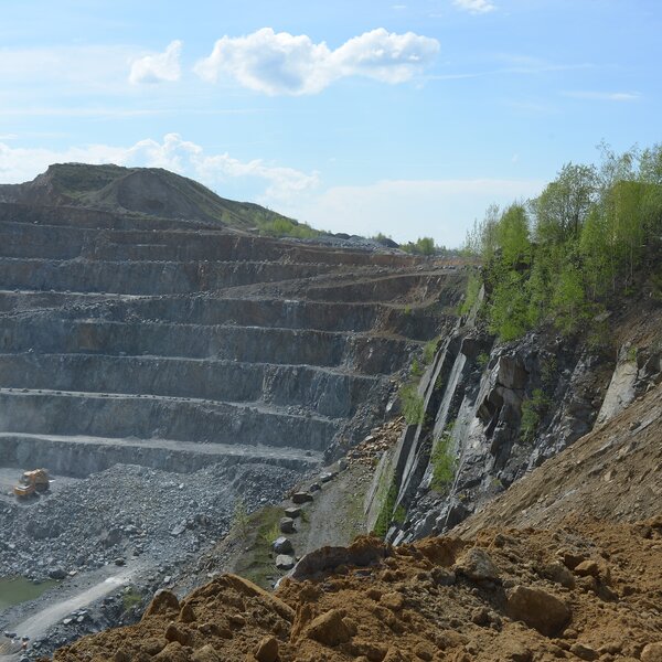Tagebausteinbruch mit stufenförmigen Abbauterrassen und einem Baufahrzeug in der Grubensohle