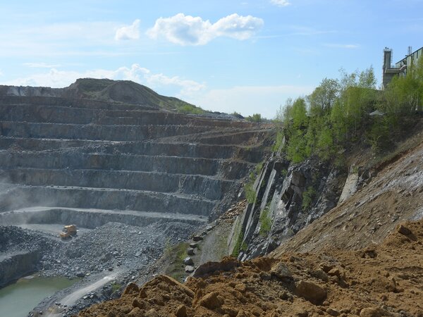 Tagebausteinbruch mit stufenförmigen Abbauterrassen und einem Baufahrzeug in der Grubensohle